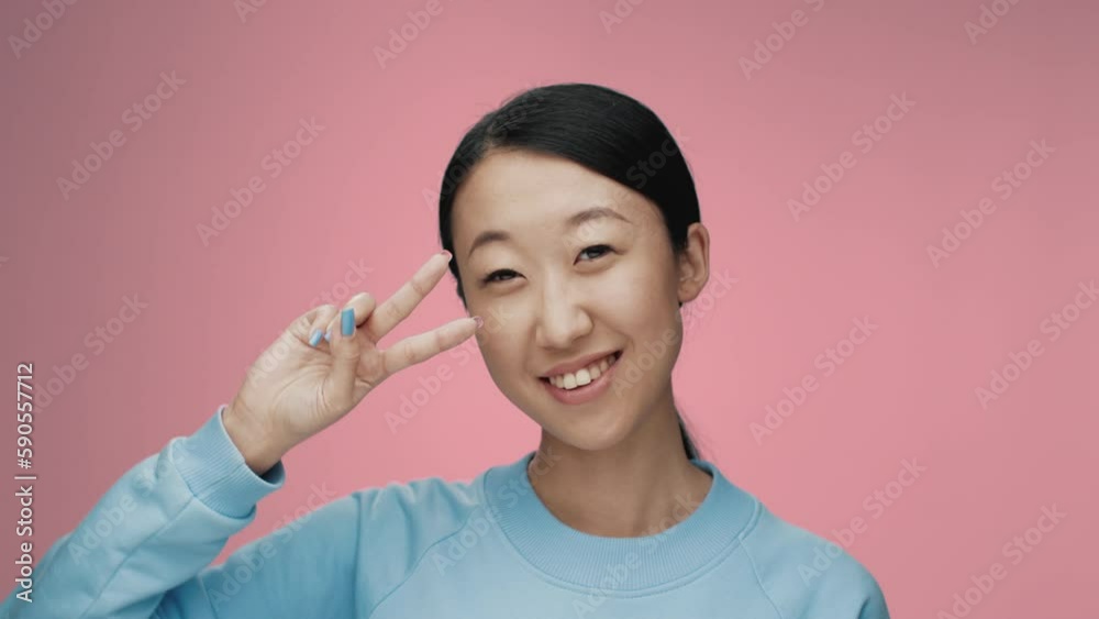 Portrait of Young Korean Woman Looking at Camera in Color Studio Shot. Adult Japanese Girl Isolated Alone on Pink Background Close up. Happy 20s Asian Person Smiling and Showing Peace Sign by Fingers Portrait of Young Korean Woman Looking at Camera in Color Studio Shot. Adult Japanese Girl Isolated Alone on Pink Background Close up. Happy 20s Asian Person Smiling and Showing Peace Sign by Fingers