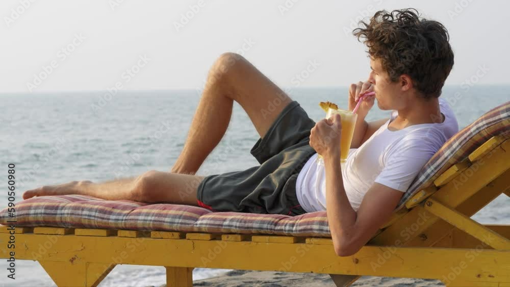 Guy is lying on a chaise longue and drinking a cocktail