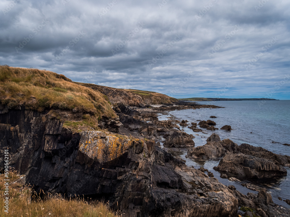 Picturesque Irish seaside landscape. Wild vegetation grows on stony soil. Cloudy sky over the ocean coast. Views on the wild Atlantic way, hills, clouds.