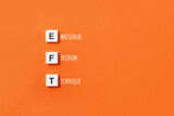 Words Emotional Freedom Technique from plastic blocks and inscriptions on orange background. Minimal concept of EFT. Selective focus, copy space