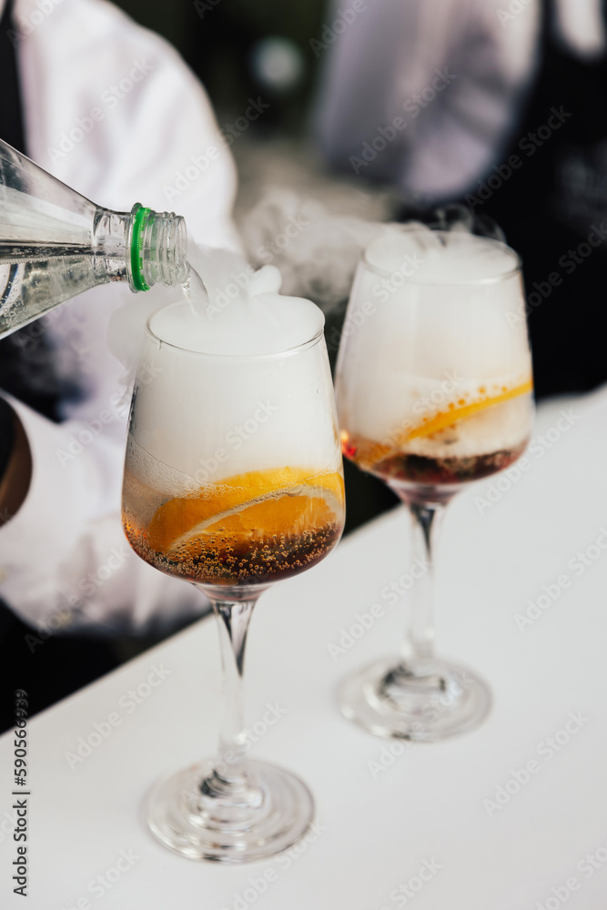 Two glasses of cocktails on the table in the bar. Bartender pours a sprite in glass. Two glasses of cocktails on the table in the bar. Bartender pours a sprite in glass.