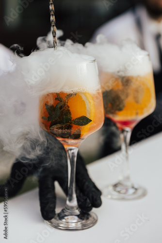 Bartender making Aperol spritz cocktail. Interferes prosecco and Aperol into a wine glass filled with ice cubes and slice of orange.