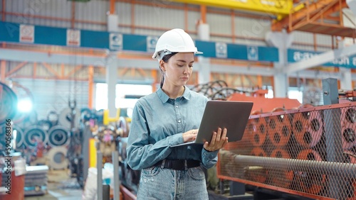 Engineer manager leader woman wearing helmet holding laptop standing and check in workplace area at manufacturing factory. Factory and Industrial plant concept