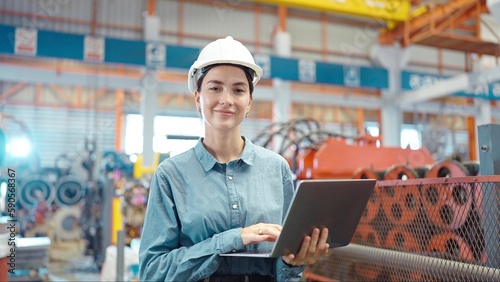 Close up smiling face of engineer manager leader woman wearing helmet holding laptop looking at camera at manufacturing factory