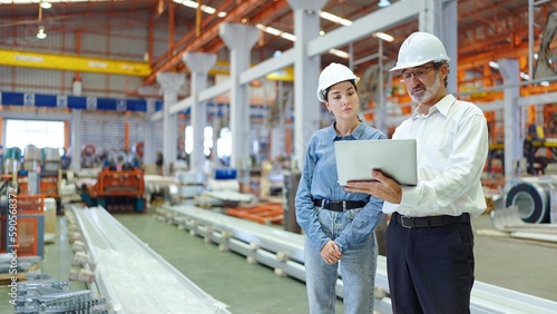 Two professional engineer man and woman manager leader wearing helmet and holding laptop standing in factory talking and discussing for work