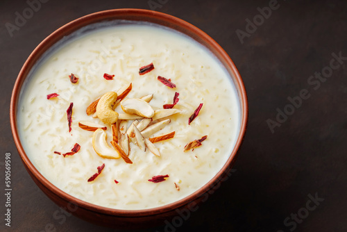 Creamy rice Kheer garnished with nuts and hibiscus. Bowl with rice pudding on dark background. Top view