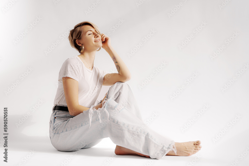 Full body of young barefoot female sitting on floor while relaxing against white background Full body of young barefoot female sitting on floor while relaxing against white background