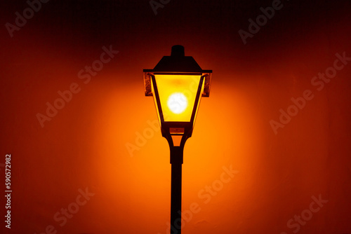 Um poste com uma luminária vintage de iluminação pública, acesa, durante a noite. photo