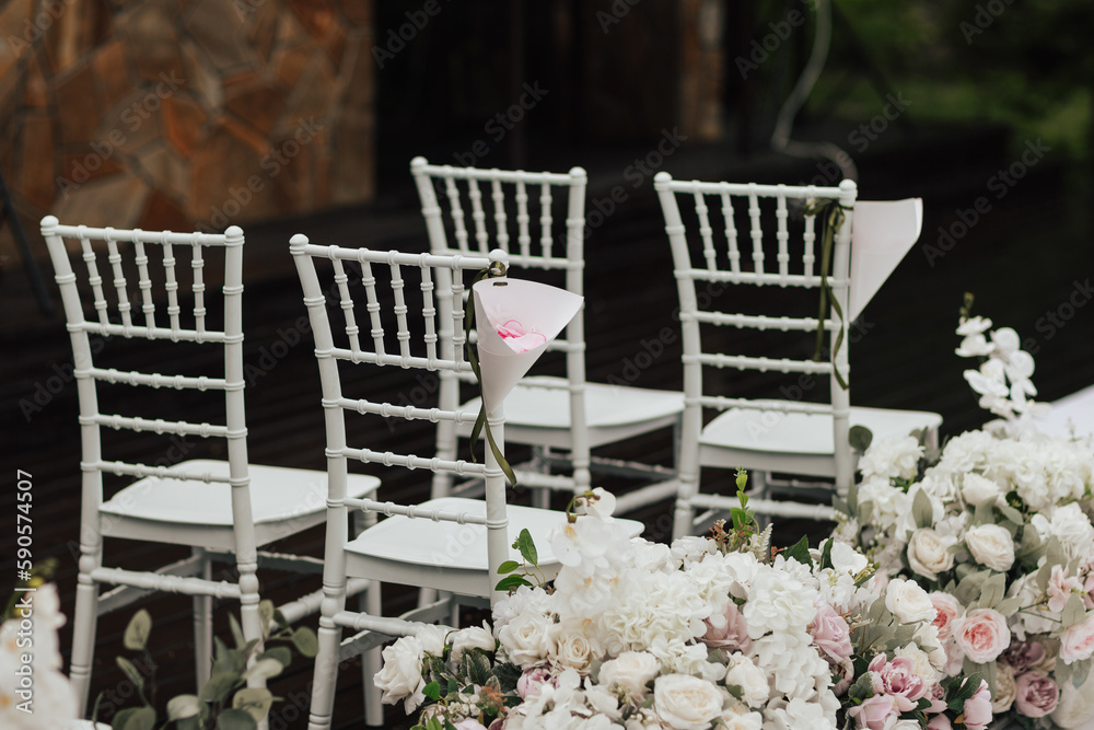 Close-up white chairs decorated with white and pink flowers roses and peony preparation for a wedding ceremony outdoor in the park forest.