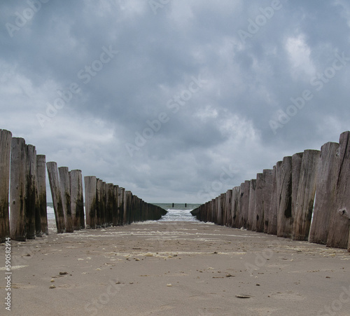 Eine Doppelreihe Holzpolder führt den Blick zur Nordsee unter einem düsteren Wolkenhimmel