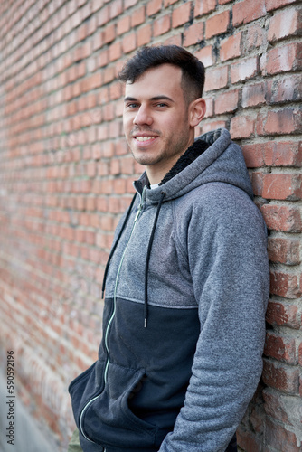 Fotografie Young caucasian man exudes coolness, leaning against a brick wall in the street