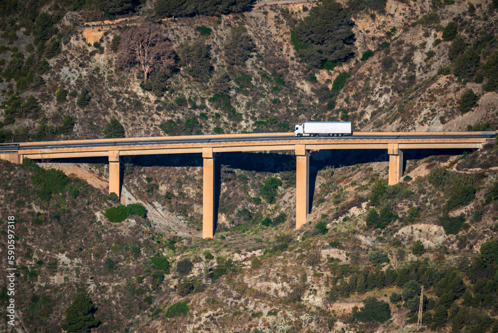 Truck with refrigerated trailer driving through a viaduct between mountains, aerial view. Truck with refrigerated trailer driving through a viaduct between mountains, aerial view.