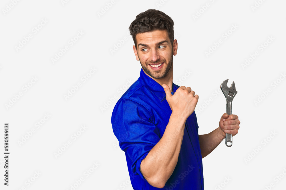 Young mechanic man holding a wrench points with thumb finger away, laughing and carefree. Young mechanic man holding a wrench points with thumb finger away, laughing and carefree.