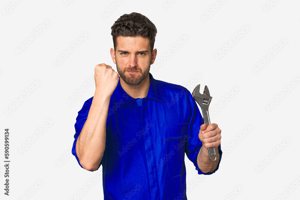 Young mechanic man holding a wrench showing fist to camera, aggressive facial expression. Young mechanic man holding a wrench showing fist to camera, aggressive facial expression.