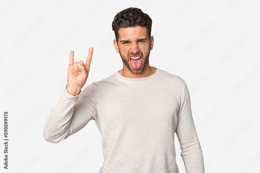 Young handsome man isolated showing a horns gesture as a revolution concept. Young handsome man isolated showing a horns gesture as a revolution concept.