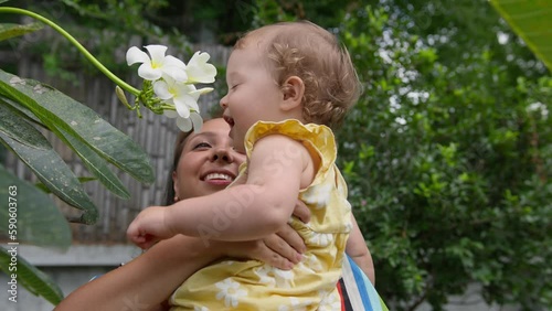 Cute baby girl smells flower during walk in garden with mom. Mother and daughter happy family moments together on travel holiday vacation