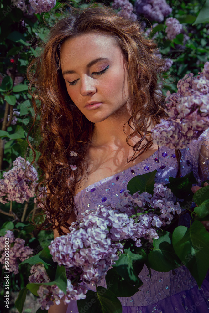 Spring style. A young woman in a beautiful dress in a garden with blooming purple bushes. Blooming spring garden.
