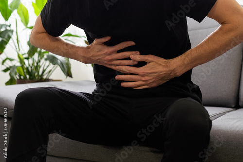 Man suffering with severe stomach pain sitting at home. Hand of mature guy holding abdomen suffering from ache, diarrhea or indigestive problem. Caucasian guy pressing on belly on painful sensation