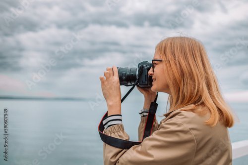 Photography and travel. Young woman in hat holding camera sitting on wooden fishing pier with beautiful tropical sea view. High quality photo