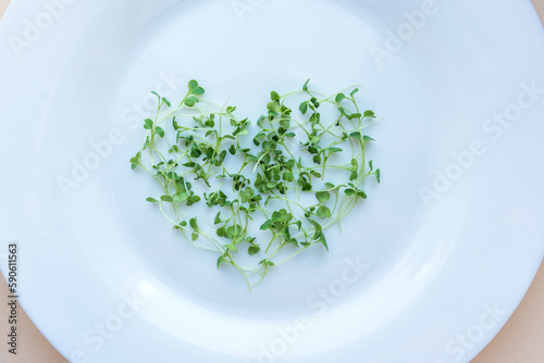 Young micro greens on a white plate in the form of a heart.