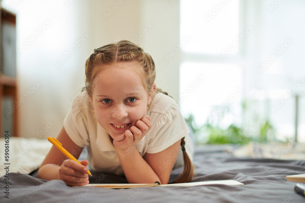 Smiling preteen girl lying on bed and writing in her diary Smiling preteen girl lying on bed and writing in her diary