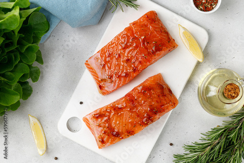 Marinated Salmon with sauce, red marinade, spicy. Fish steaks, slices. Raw uncooked salmon fillet fish with rosemary, lemon and pepper on white cutting board and grey background.
