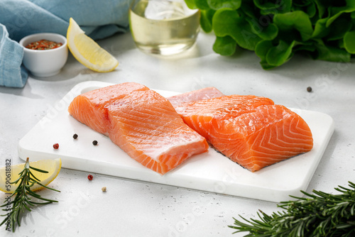 Salmon. Fish steaks, slices. Raw uncooked salmon fillet fish with rosemary, lemon and pepper on white cutting board and grey background.