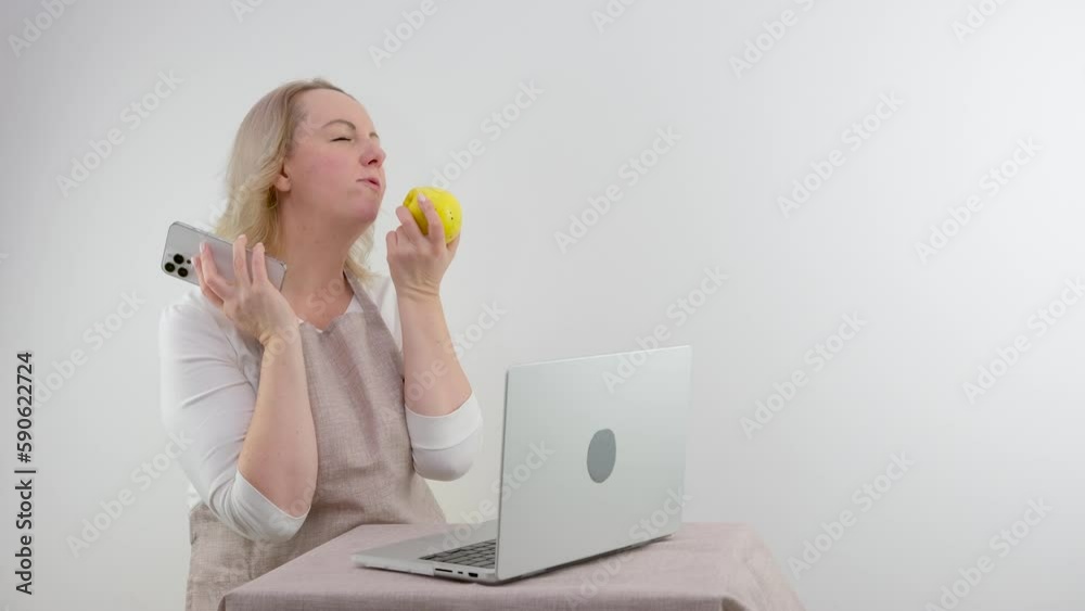 housewife cooks food looks at recipes on computer on internet and talks on phone and eats apple on white background space for text cooking cooking delicious food diet nutritionist communicating