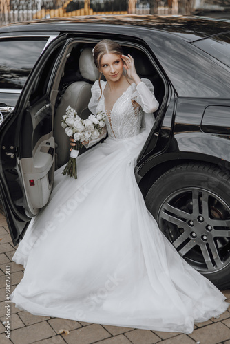gorgeous bride with trendy makeup and hairdo in luxury wedding dress in black wedding car sitting on back seat and posing for photographer © Vasil