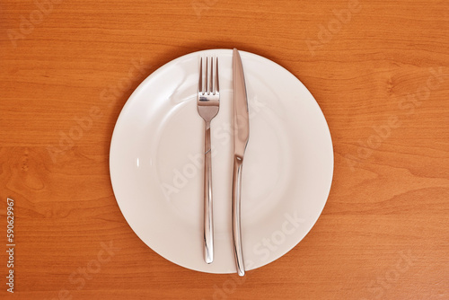 A signal  The dish is wonderful . Empty and clean white plate with fork and knife on a wooden table as an example of table etiquette