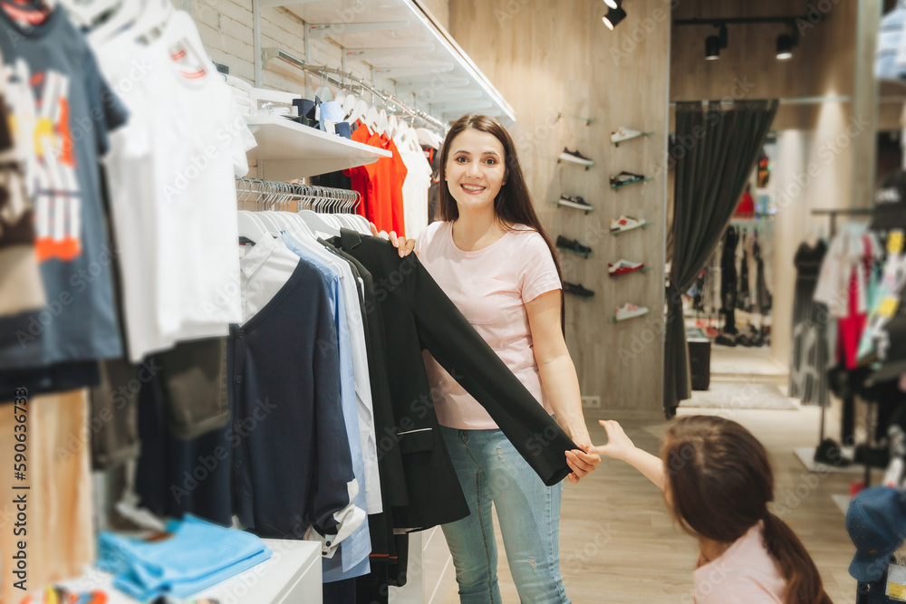 mother and daughter buy clothes. mother and little girl trying on clothes in the shop mother and daughter buy clothes. mother and little girl trying on clothes in the shop