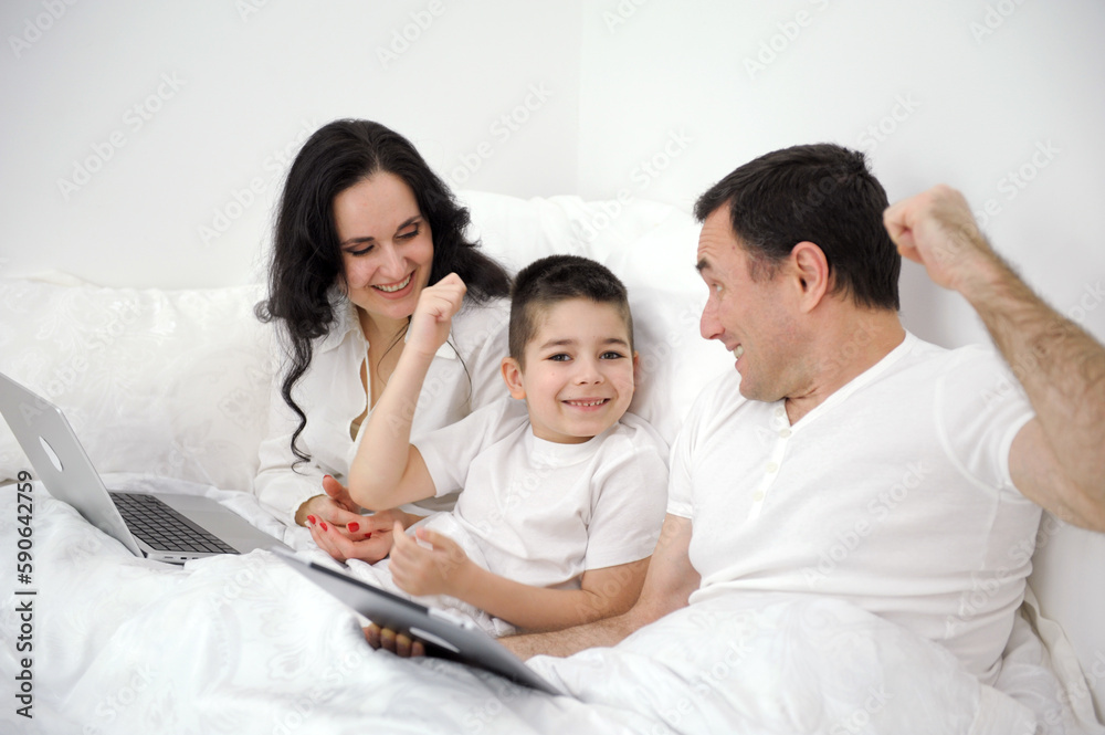 husband wife in bed with little son looking at tablet cartoon interesting game pictures laughing talking communication real people at home love life happy family with tablet pc in bed at home husband wife in bed with little son looking at tablet cartoon interesting game pictures laughing talking communication real people at home love life happy family with tablet pc in bed at home