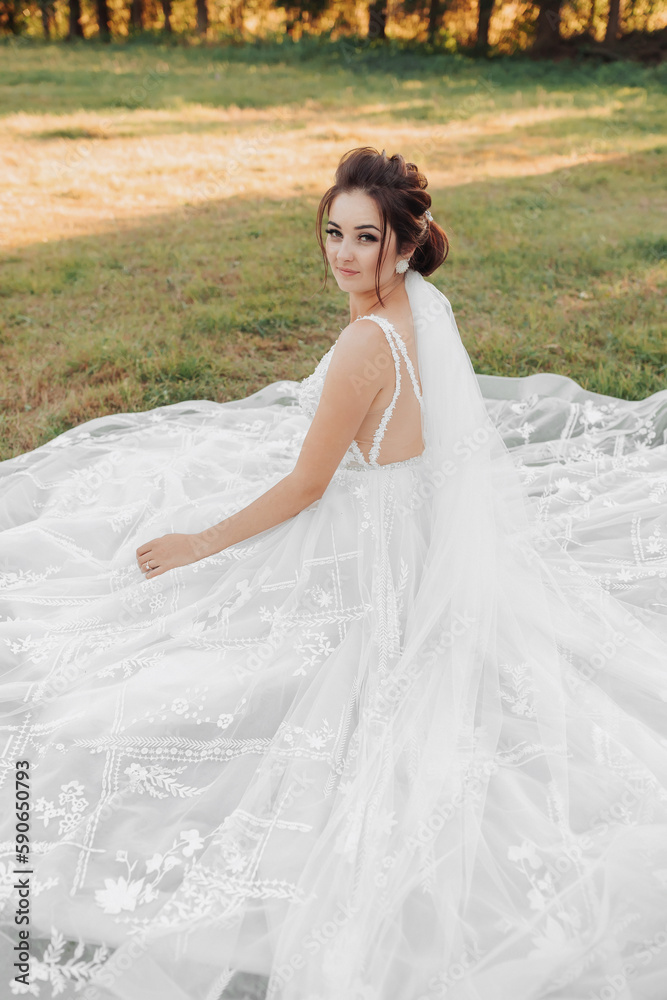 Wedding portrait of the bride. A beautiful bride is sitting in a white dress on the green grass and looking over her shoulder into the camera lens. Green background. Beautiful makeup. A young girl.