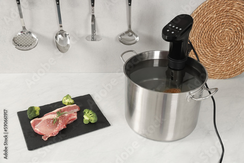 Pot with sous vide cooker and ingredients on table in kitchen. Thermal immersion circulator photo