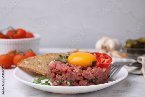 Tasty beef steak tartare served with yolk, pepper, bread and greens on white marble table