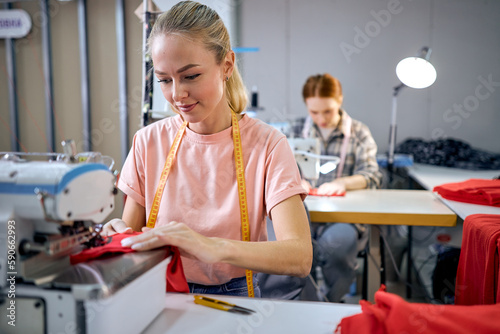 focus on pleasant caucasian blonde lady using sewing machine. happy women working as seamstress in clothing factory, clothing production concept. dressmaking, tailoring in workshop