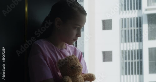 Cute little girl portrait child is sad in her room with a toy in her hands, child in depression in the room with a toy bear in his hands. Sad family. Fear of child in dark. Family violence concept. 4K