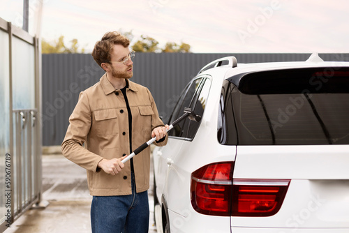 Man washing his car at self-service car wash with window scraper. Concept care of vehicle