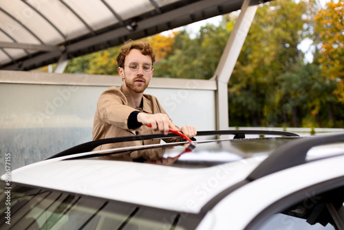 Handsome man cleaning a car with window cleaner wiper. Washing car concept