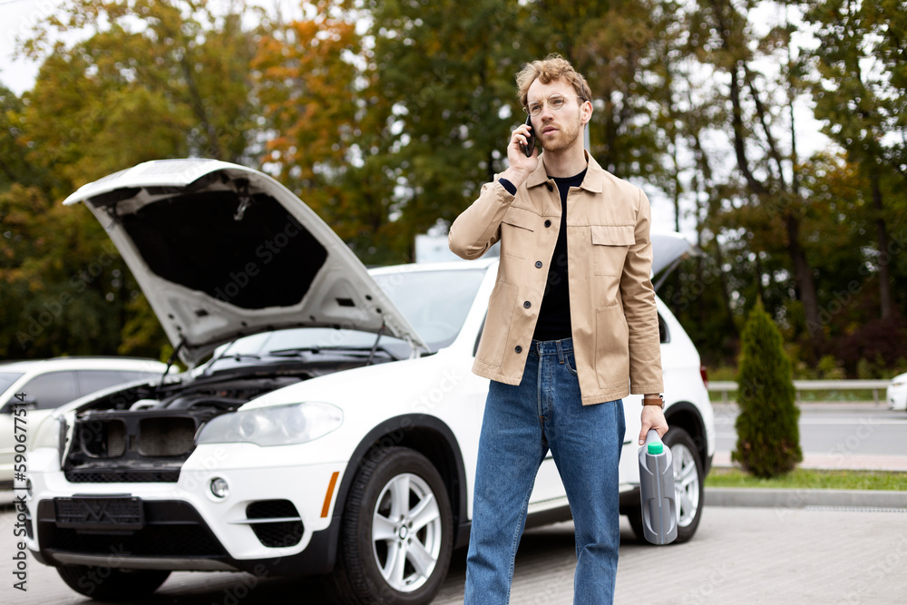 Pensive male standing near car with hood open, talking on smartphone. Car service concept