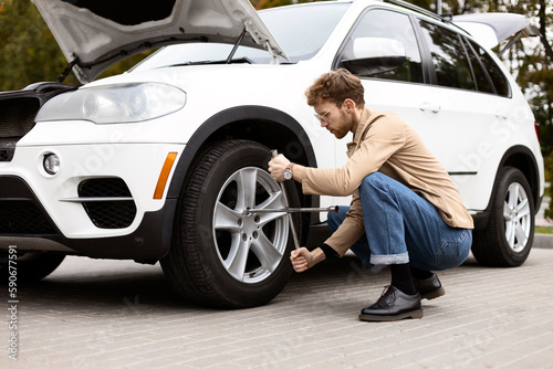 Pensive man changes tire on SUV outdoors. Car repair concept © Maria Vitkovska