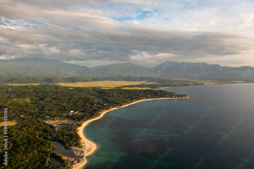 Aerial drone of coastline with a beach during sunset against the backdrop of mountains. Pagudpud, Ilocos Norte, Philippines.