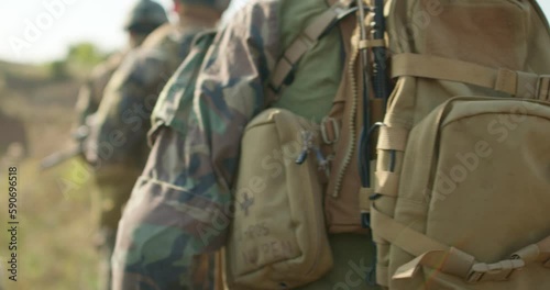 young fully equiped men marching walking along field road In Autumn Day. Group of Soldiers Marching In Forest. back view slow motion
