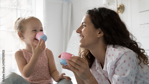 Photography Happy mom and joyful kid playing learning game at home, pretending drinking tea, coffee from toy plastic tiny cups, talking, laughing, enjoying funny leisure, family playtime