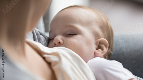 New mom breastfeeding calm peaceful sleepy infant with closed eyes, holding sleeping little baby in arms. Adorable hungry innocent child sucking, drinking milk from mothers breast. Close up shot