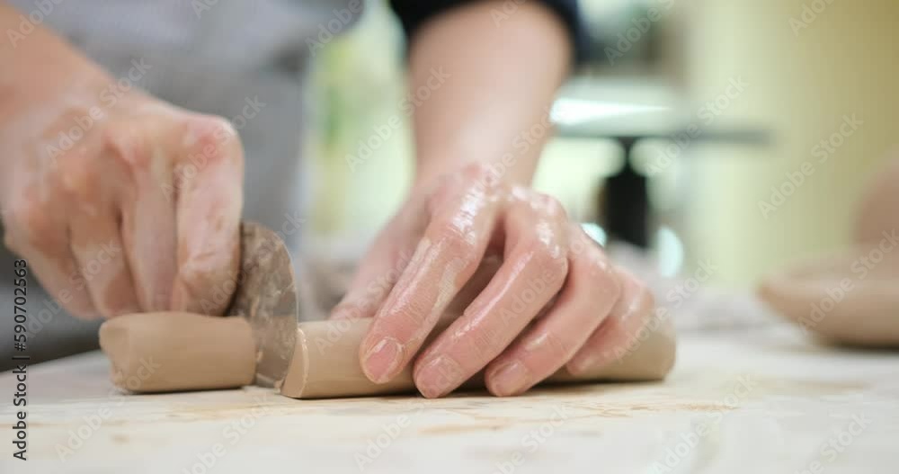 Woman cutting clay with blade standing behind table in studio Woman cutting clay with blade standing behind table in studio