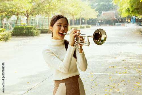 Canvas Print Beautiful asian teacher using sound power standing blowing instrument playing trumpet beautiful jazz instrument smiling good mood in front of school building : Jazz music improves mental health