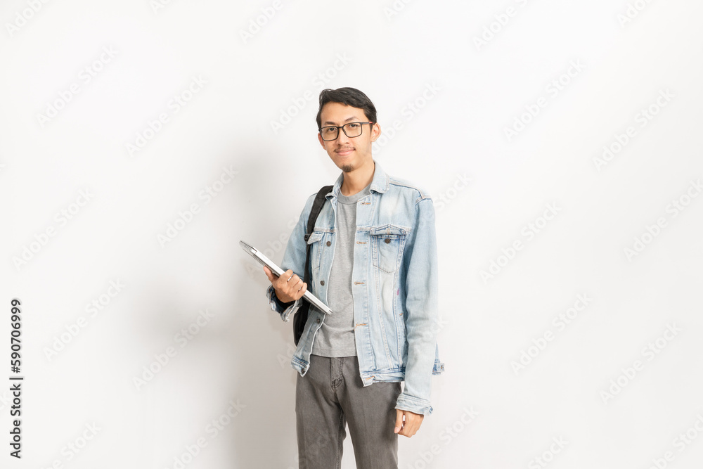 A college student with his laptop and backpack gives confident look. Indonesian or southeast asian model isolated with white wall background. A college student with his laptop and backpack gives confident look. Indonesian or southeast asian model isolated with white wall background.