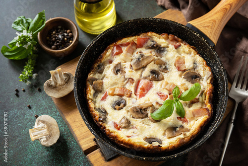 Omelette with mushrooms and bacon on a dark stone table. Frittata is an Italian breakfast dish.