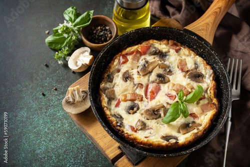 Frittata is an Italian breakfast dish. Omelette with mushrooms and bacon on a dark stone table. Copy space.